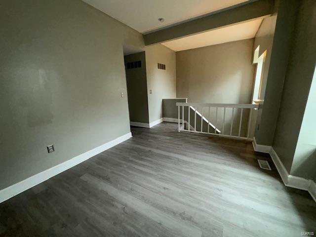 unfurnished room featuring visible vents, beamed ceiling, baseboards, and wood finished floors