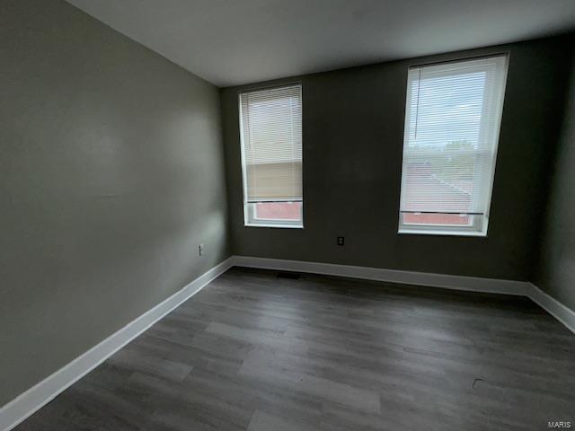 spare room featuring baseboards and dark wood-type flooring