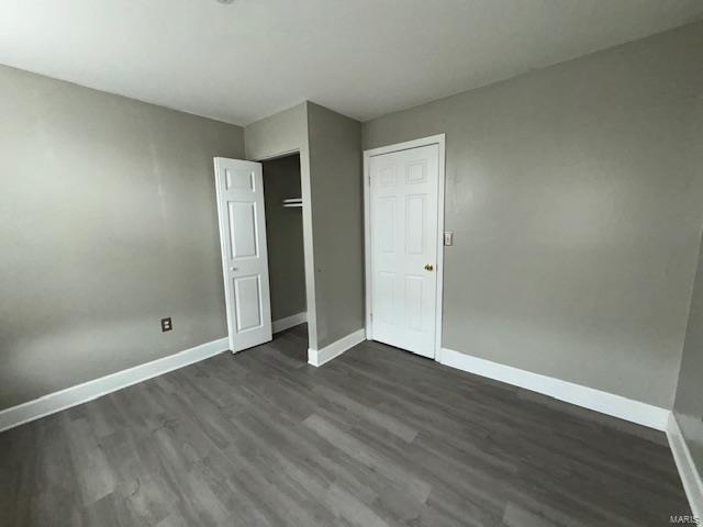 unfurnished bedroom with a closet, dark wood finished floors, and baseboards