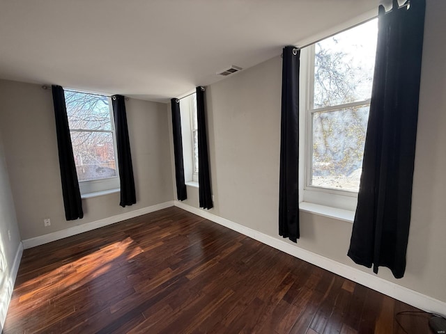 empty room featuring dark wood-type flooring, visible vents, and baseboards