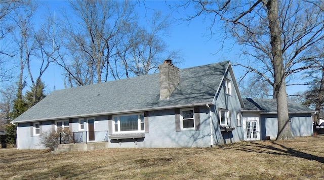 view of front facade with a front yard, brick siding, a chimney, and roof with shingles