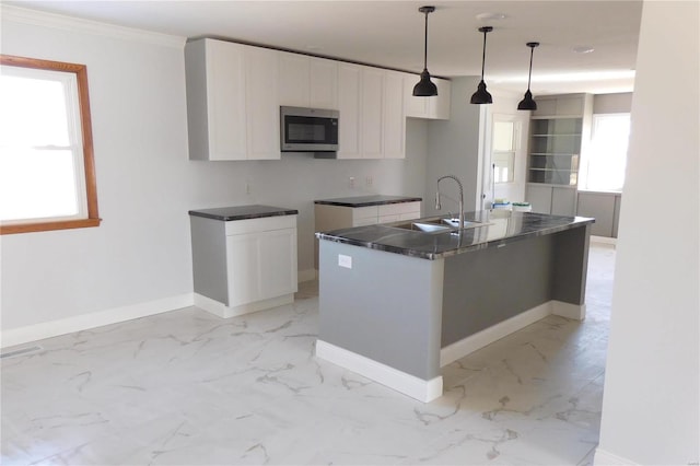 kitchen featuring a sink, white cabinetry, an island with sink, stainless steel microwave, and pendant lighting