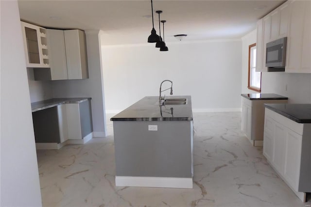 kitchen with dark countertops, glass insert cabinets, hanging light fixtures, marble finish floor, and a sink