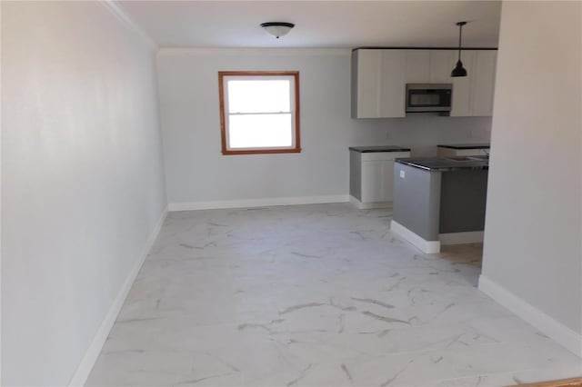 kitchen featuring pendant lighting, marble finish floor, dark countertops, stainless steel microwave, and white cabinetry