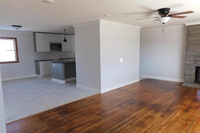 unfurnished living room featuring crown molding, a stone fireplace, baseboards, and wood finished floors