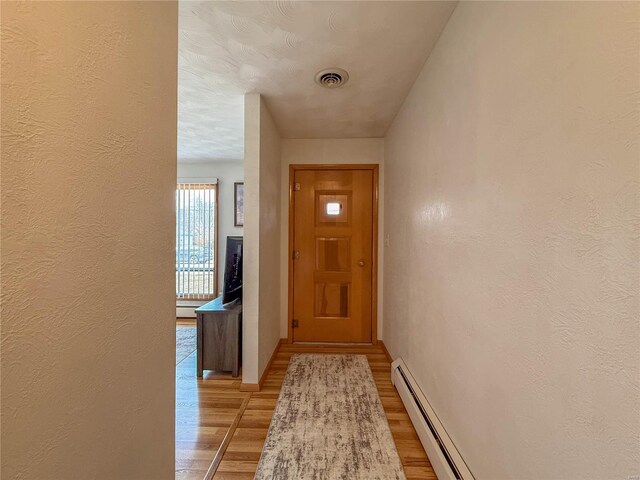 entryway featuring a baseboard heating unit, light wood-type flooring, visible vents, and a textured wall