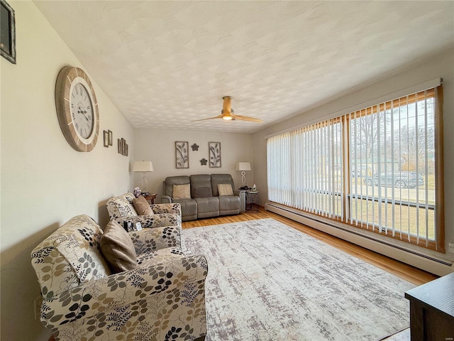 living area with a textured ceiling, a baseboard radiator, wood finished floors, and a ceiling fan