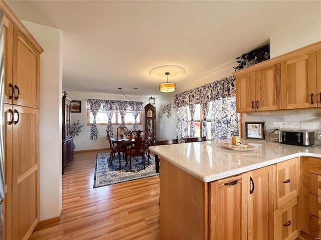 kitchen with a toaster, light stone counters, a peninsula, light wood-type flooring, and backsplash