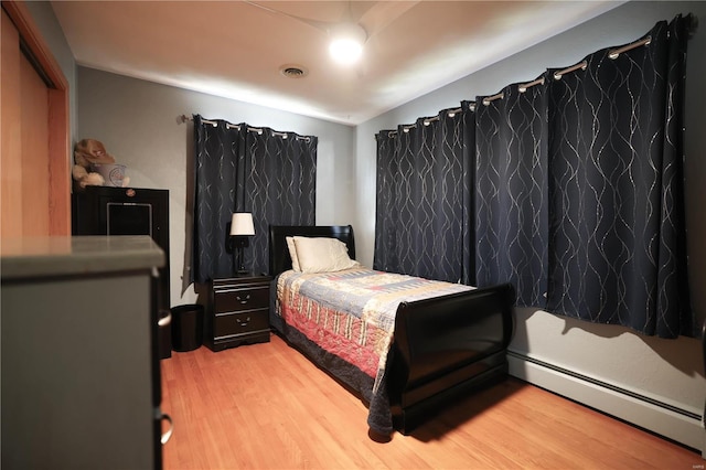 bedroom with a baseboard heating unit, lofted ceiling, visible vents, and light wood-style floors