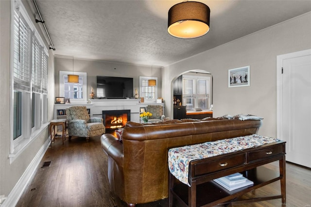 living area featuring a warm lit fireplace, a textured ceiling, arched walkways, wood finished floors, and visible vents