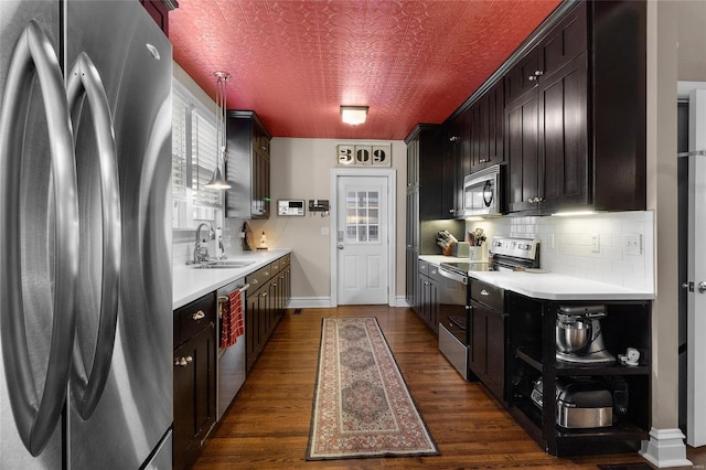 kitchen featuring stainless steel appliances, a sink, light countertops, backsplash, and dark wood-style floors