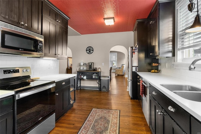 kitchen with arched walkways, light countertops, appliances with stainless steel finishes, and a sink