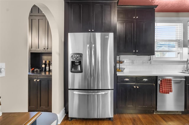 kitchen featuring arched walkways, appliances with stainless steel finishes, wood finished floors, light countertops, and backsplash