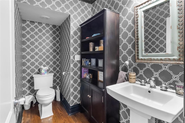 bathroom featuring toilet, wallpapered walls, a sink, and wood finished floors