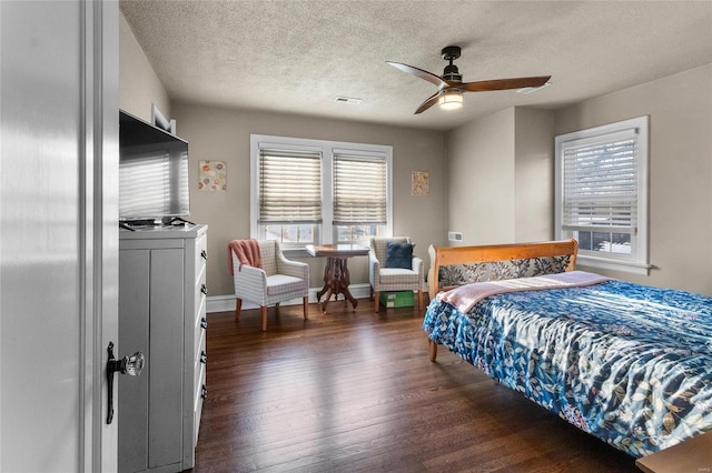 bedroom with a textured ceiling, ceiling fan, dark wood-type flooring, and multiple windows