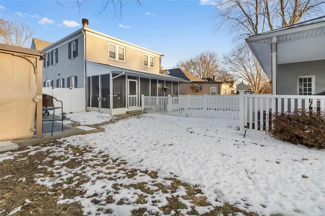 snow covered back of property with a sunroom and a fenced backyard