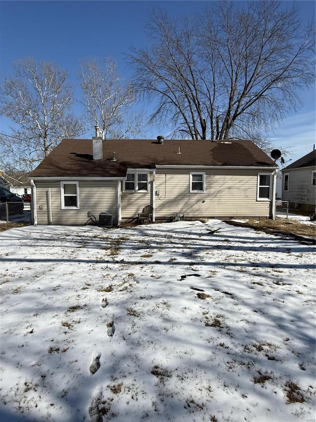 snow covered back of property featuring cooling unit and a chimney