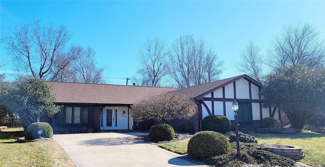 tudor house with driveway, a shingled roof, and brick siding