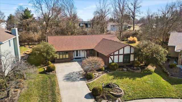 tudor house with a front yard, concrete driveway, and brick siding