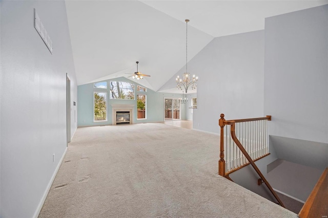 unfurnished living room with carpet floors, a glass covered fireplace, high vaulted ceiling, baseboards, and ceiling fan with notable chandelier