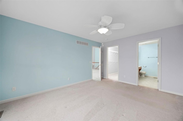 unfurnished bedroom with a walk in closet, a closet, visible vents, light carpet, and baseboards