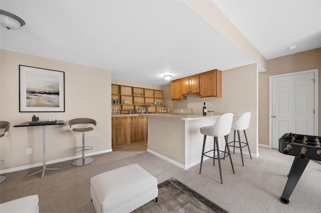 kitchen featuring a breakfast bar area, light colored carpet, a peninsula, light countertops, and brown cabinetry