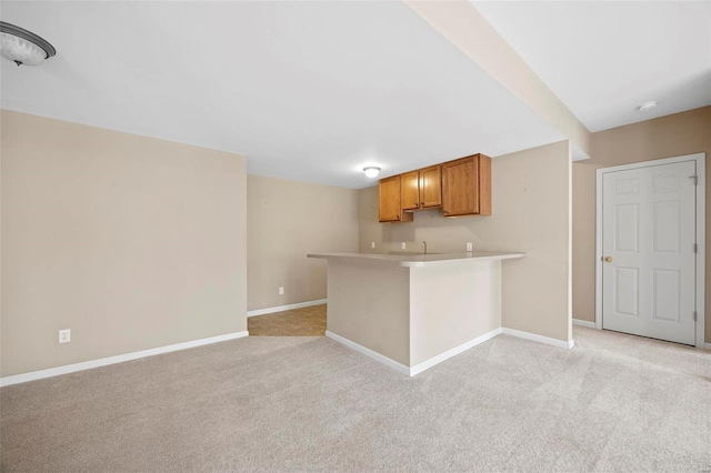 kitchen featuring light carpet, baseboards, brown cabinets, a peninsula, and light countertops