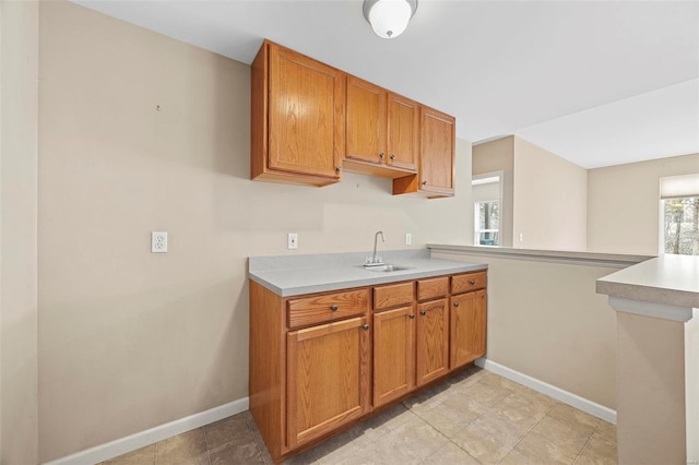 kitchen with baseboards, brown cabinetry, a peninsula, light countertops, and a sink