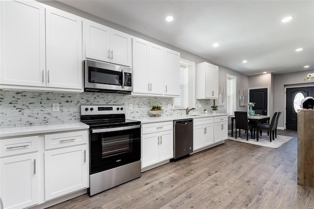 kitchen featuring tasteful backsplash, appliances with stainless steel finishes, light wood-style floors, white cabinetry, and a sink