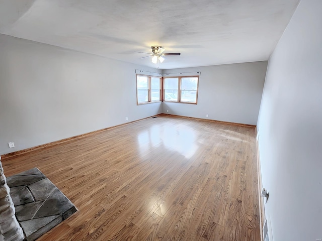 empty room featuring a ceiling fan, baseboards, and light wood finished floors