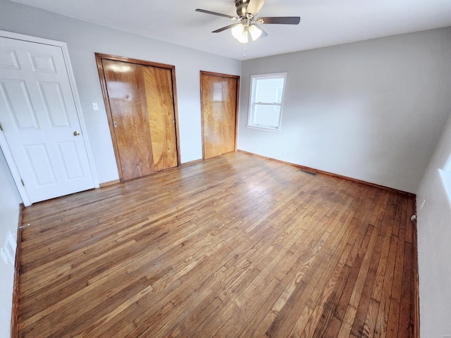 unfurnished bedroom with baseboards, visible vents, ceiling fan, wood finished floors, and two closets