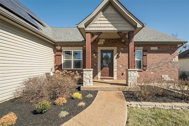 view of exterior entry featuring brick siding and a shingled roof