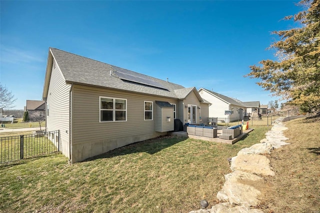 rear view of house featuring a yard, solar panels, a fenced backyard, and a shingled roof