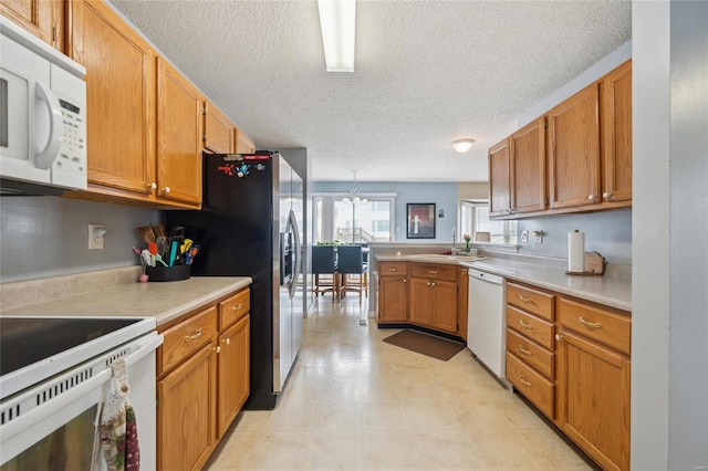 kitchen featuring a peninsula, white appliances, a sink, light countertops, and brown cabinetry