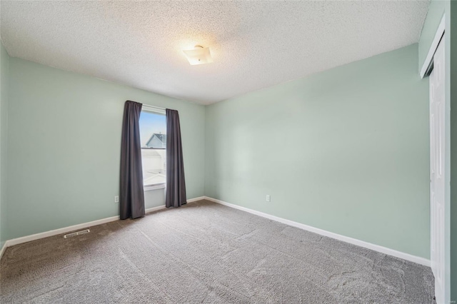 carpeted spare room featuring visible vents, baseboards, and a textured ceiling