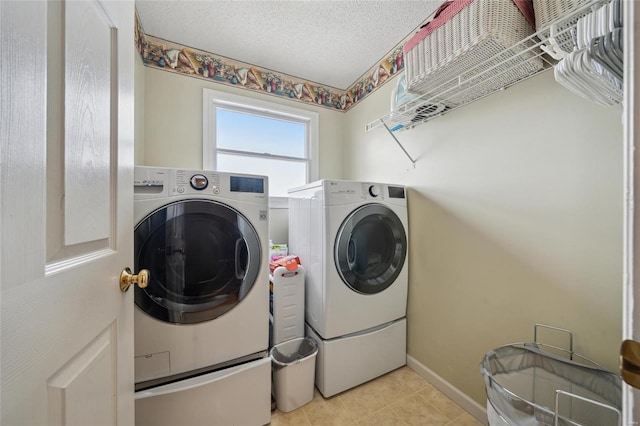 clothes washing area with a textured ceiling, light tile patterned floors, laundry area, baseboards, and washing machine and clothes dryer