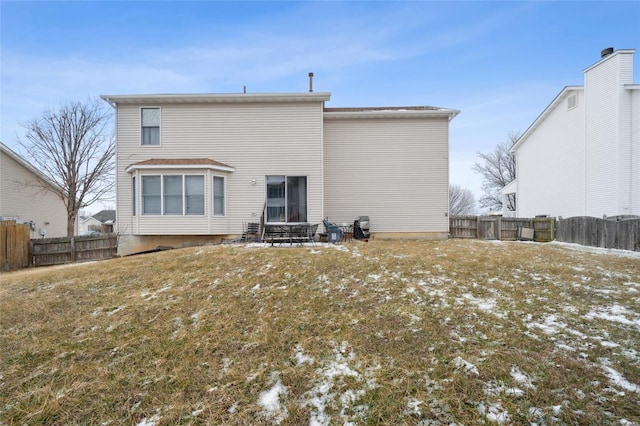 snow covered back of property featuring a fenced backyard and a yard