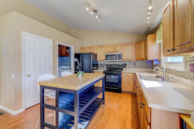 kitchen featuring washer / dryer, tasteful backsplash, vaulted ceiling, black appliances, and a sink