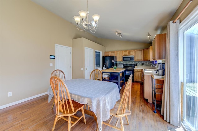 dining room with lofted ceiling, light wood finished floors, baseboards, and an inviting chandelier