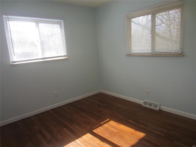 empty room featuring a healthy amount of sunlight, visible vents, baseboards, and wood finished floors