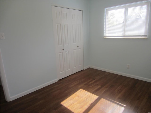 unfurnished bedroom featuring dark wood-type flooring, a closet, and baseboards