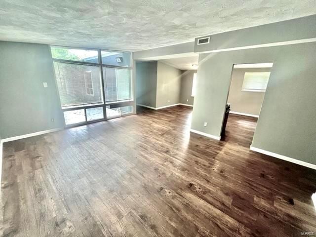 spare room with a textured ceiling, dark wood-style flooring, visible vents, baseboards, and expansive windows