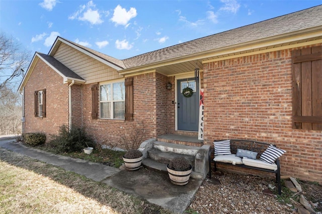 view of exterior entry featuring roof with shingles and brick siding