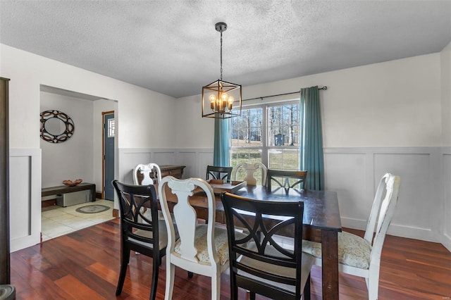 dining area featuring a wainscoted wall, a textured ceiling, an inviting chandelier, and wood finished floors