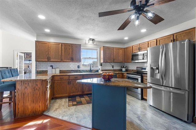 kitchen featuring a breakfast bar area, appliances with stainless steel finishes, brown cabinetry, a sink, and a peninsula