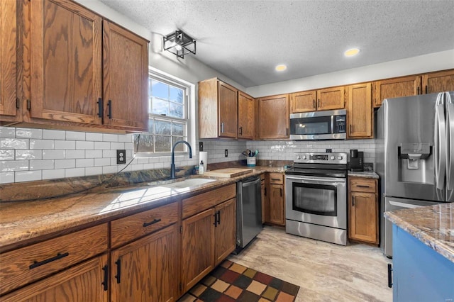 kitchen with stainless steel appliances, tasteful backsplash, brown cabinetry, a sink, and a textured ceiling