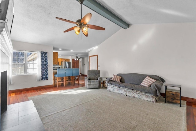 living room featuring a fireplace, vaulted ceiling with beams, a textured ceiling, and baseboards