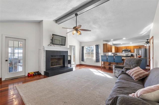 living room featuring lofted ceiling with beams, dark wood-type flooring, a textured ceiling, and a tiled fireplace