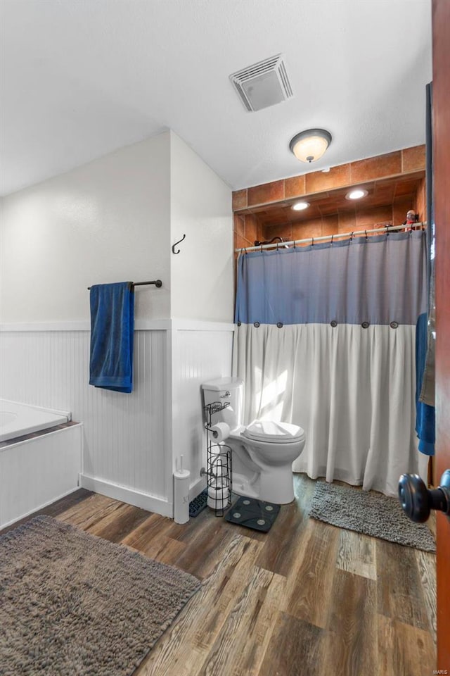 bathroom featuring visible vents, a shower with shower curtain, toilet, a wainscoted wall, and wood finished floors