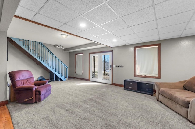 carpeted living room featuring a drop ceiling, baseboards, and stairs